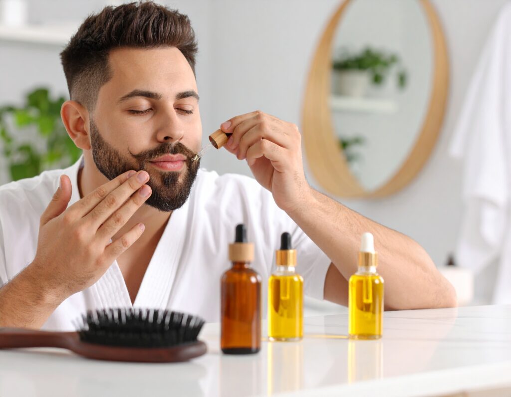 hands applying beard oil to a freshly trimmed moustache, with grooming products including oil bottle and comb visible on a marble bathroom counter